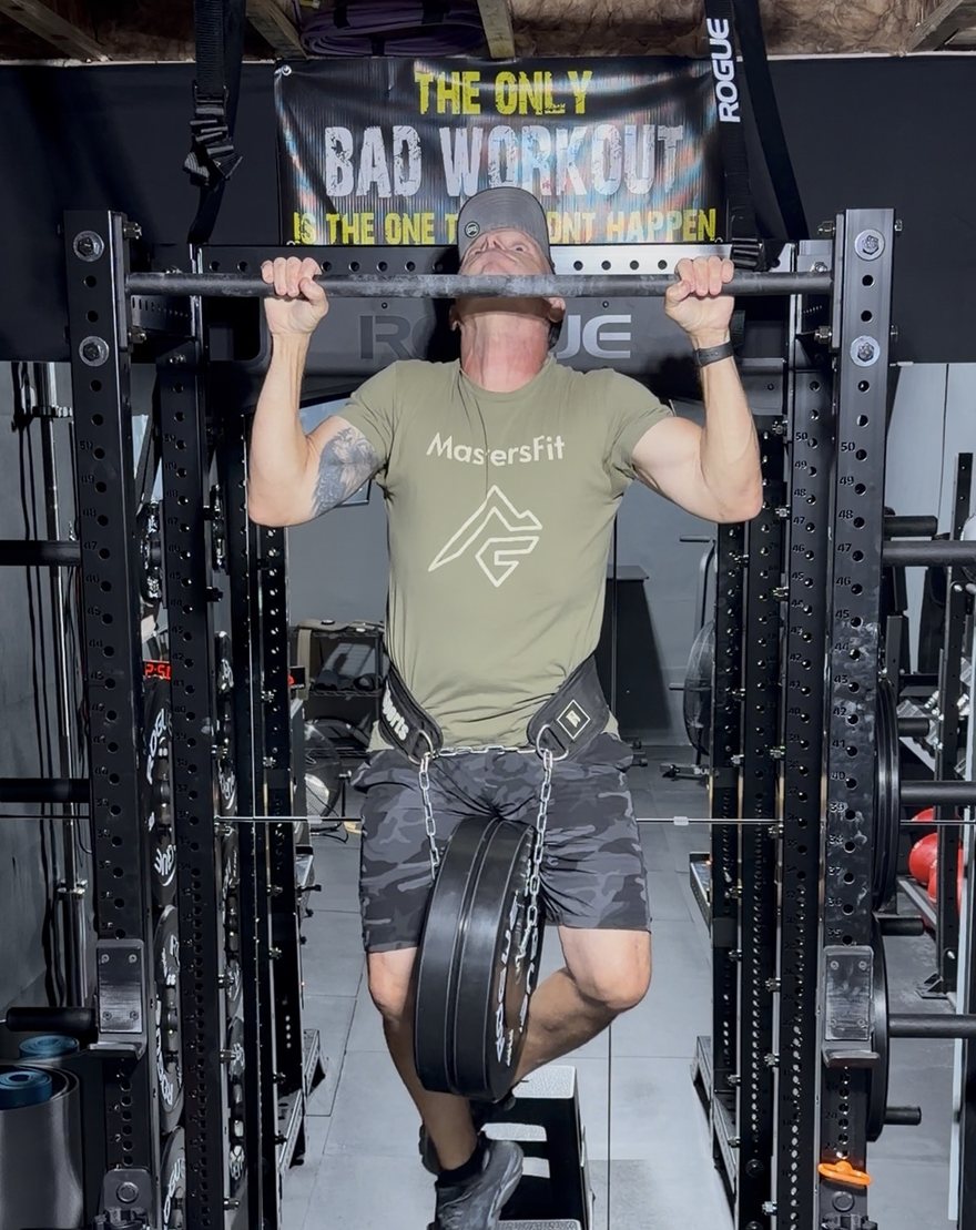Rich Pusateri, founder of MastersFit, doing a pull-up with 90 lbs of plates hanging from a dip belt